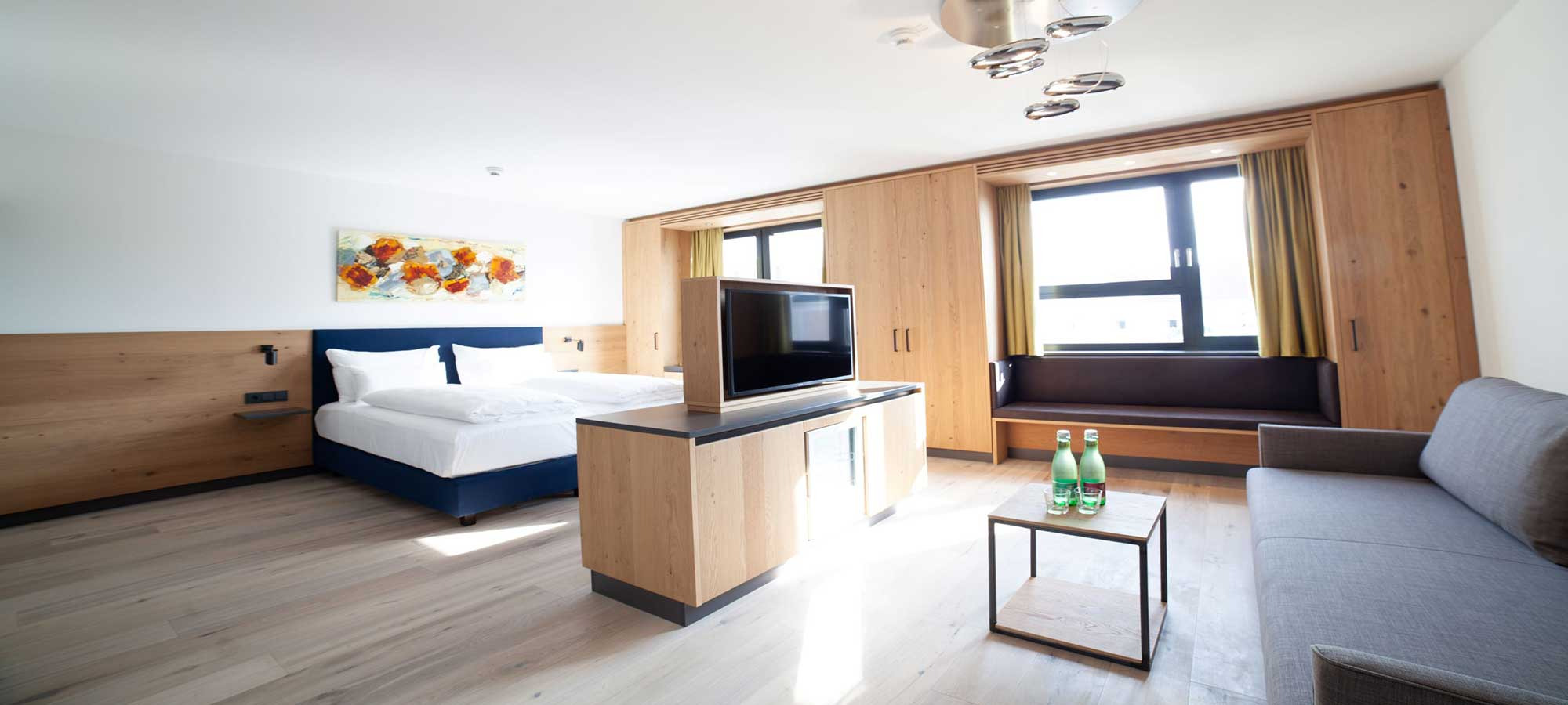  Modernes Hotelzimmer mit Doppelbett, Sofa, Fernseher und großen Fenstern.